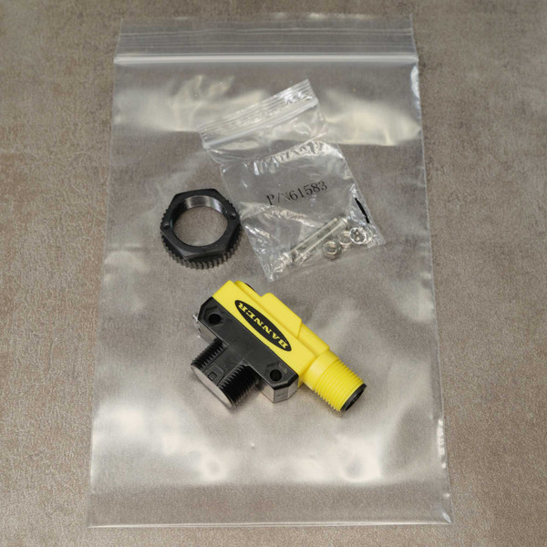 Banner sensor with yellow housing, black bracket, knurled lock nut, and hardware bag labeled P/N61583 — complete, unused, no visible wear.