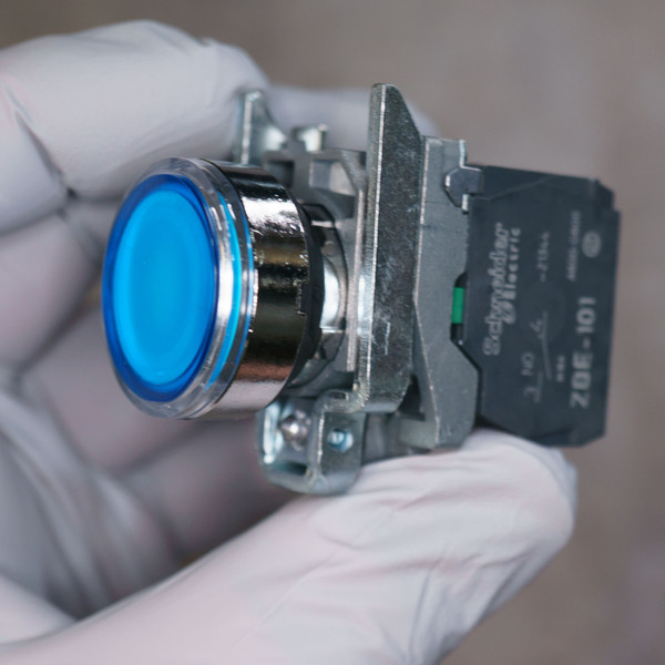 Blue flush illuminated cap, chrome metal body, ZBE-101 NO contact block attached. Green terminal visible. No damage observed.