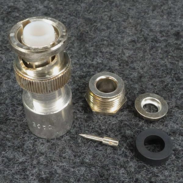 Disassembled connector showing main body with knurled coupling ring and white dielectric insert, threaded bushing, center pin, washer, and rubber grommet. Stamped code visible on body.