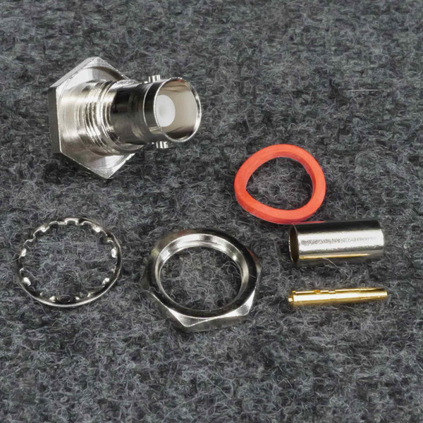 Five-piece connector kit laid out: nickel body with square flange and white dielectric, hex locknut, star washer, red O-ring, gold-pin contact with silver ferrule.