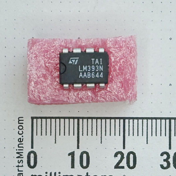 Top view of STMicroelectronics LM393N IC in pink foam next to a millimeter ruler.