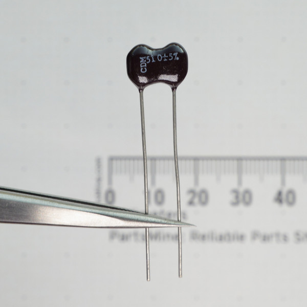 Close-up of Cornell Dubilier CD15D511J03 dipped mica capacitor held in tweezers.