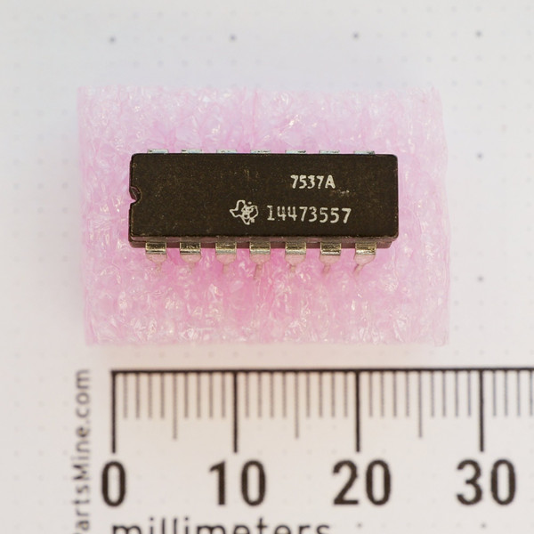 Texas Instruments 14473557 DIP-14 integrated circuit on pink foam with millimeter ruler.