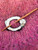 inlaid shell shawl pin in the shape of a sheep featuring a brown face, white fleece, and black eyes. A coconut wood stick to hold the pin in place completes the set.
