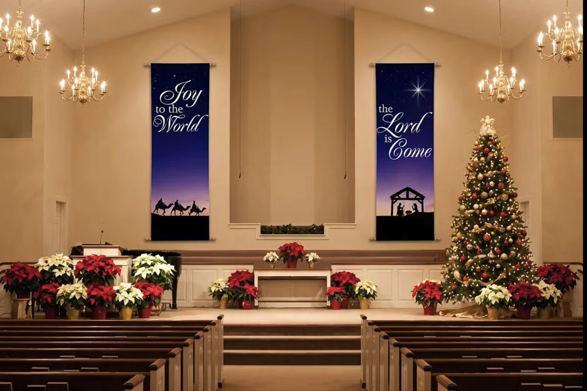 NXM010 Nativity Scene banner set with Joy to the World and The Lord Is Come fabric banners hanging on either side of a church stage decorated with poinsettias and a Christmas tree