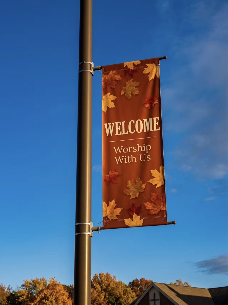 Fall Welcome light pole banner with autumn leaves mounted high on a parking lot light pole against a blue sky