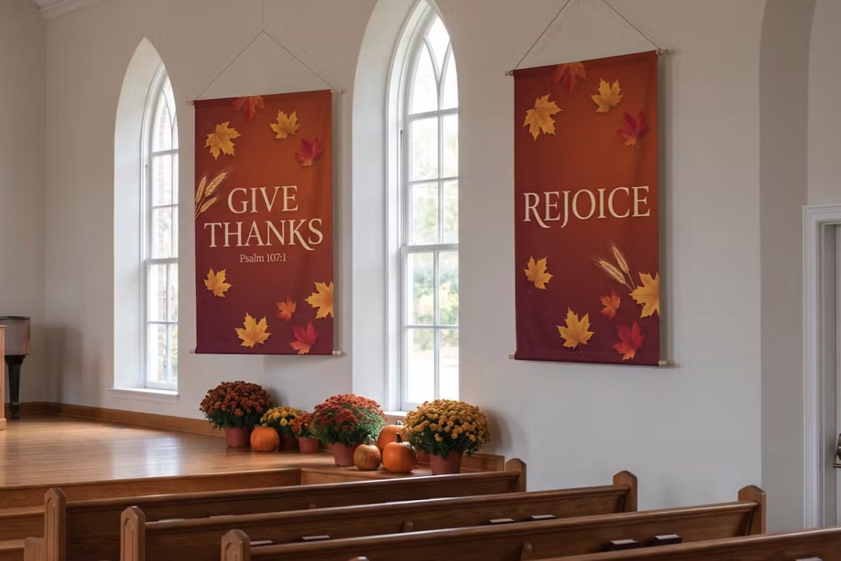 Two fall fabric church banners reading Give Thanks and Rejoice hanging on a sanctuary wall with mums and pumpkins along the stage