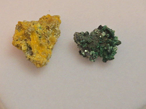 green Torbernite & yellow Parsonsite thumbnail sized specimens on display under indoor light