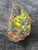 yellow splotchy Uranopilite after black  Uraninite  on  rust colored feldspar matrix under outdoor light