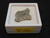 This vitreous looking trinitite specimen displayed in white plastic display case top view