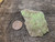 drab green Andersonite globules with rare green Schröckingerite spatters on sandstone matrix under outdoor light