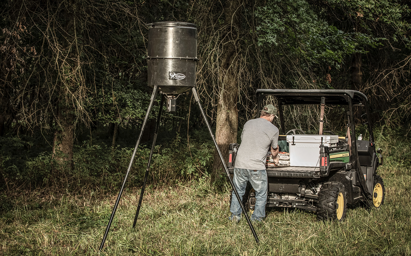 Hunter setting a tripod deer feeder to the right height in the field