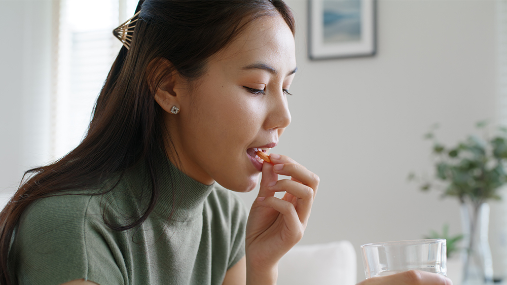 A woman in a bright kitchen takes a vitamin that could likely be folic acid to help fertility and get pregnant.