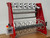 InnoPrinter RC60 DTF roll slitter, three-quarter angle view. A red powder-coated slitter showing five adjustable blade holders on the upper rail, stainless steel rollers, six aluminum separator reels on the gray rewind shaft, white control panel with red emergency stop and on/off switch, and tensioning knobs on the right end shaft.