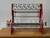 InnoPrinter RC60 DTF roll slitter, front view. A red-framed tabletop slitter with five razor blade cutting heads mounted on a top rail, multiple horizontal tension and idler rollers, six metal separator discs spaced along a gray rewind shaft, and a white control box with an emergency stop button and power switch on the left side.