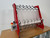 InnoPrinter RC60 DTF roll slitter threaded with white film, angled view. Red-framed slitter with six strips of white DTF film fed from the top rail down through the blade assembly and separated onto metal discs along the rewind shaft, with the InnoPrinter control box and emergency stop visible on the left.