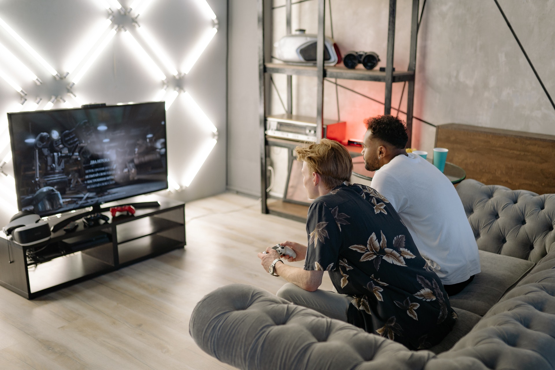 Two men playing video games whilst sat on  sofa