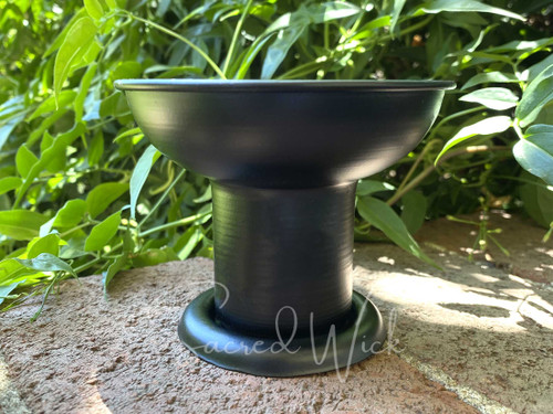 one black pedestal pillar candle holder sits on brickwork with greenery in the background