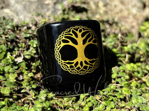 Black ceramic chime and mini taper candle holder with gold tree of life printed, resting in greenery.