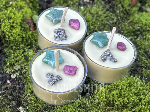 Three Winter’s Blessing Bayberry Crystal Tealights resting on moss-covered bricks, shown from the front to highlight candle depth, real bayberry wax, and the top crystals — green aventurine star, ruby chips, and pyrite accents.