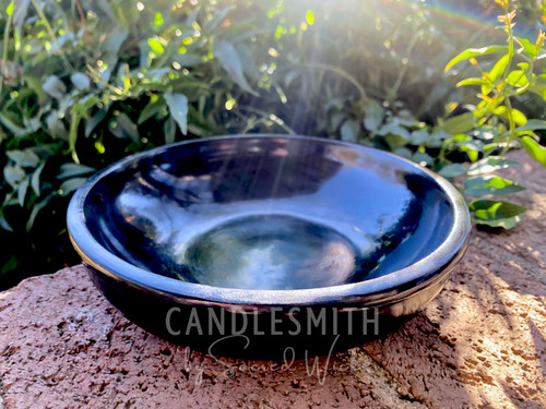 One Black Stone Shallow Incense & Candle Bowl with Polished Finish shown from the front and slightly above rests on brickwork with grenenery in the background.