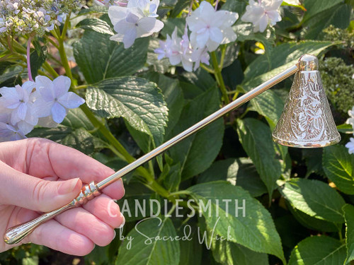 One Baroque Brass Candle Snuffer is held in hand angled to the right with greenery in the background