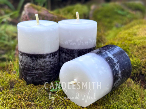Three Black and White Votive Candles are shown from the front they stand on moss covered bricks and one rests on the side.