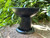 one black pedestal pillar candle holder sits on brickwork with greenery in the background