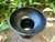 one black pedestal pillar candle holder sits on brickwork with greenery in the background shown from above.