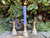 Three brass candle holders sit on a concrete pathway with clover and greenery in the rear. One candle holder demonstrated use with a light blue beeswax chime candle, which is not included.