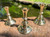 Three brass candle holders sit on brickwork in a vintage candlestick style with greenery and water behind them.