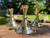 Three brass candle holders sit on brickwork in a vintage candlestick style with greenery and water behind them, shown from above slightly.