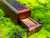 one wooden incense burner coffin box lies on a bed of moss with the storage drawer opened partially and the lid closed.