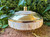 one mother of pearl and brass incense, smudge, and decorative bowl shown from the front rests on brickwork with greenery in the background.