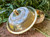 one mother of pearl and brass incense, smudge, and decorative bowl shown from the front with the lid off resting across the front of the bowl to show the detailing of the top, it lies on brickwork with greenery in the background.