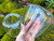 One floating handblown glass votive and tealight candle holder rests on moss-covered brick. A second candle holder is being held to show the open chamber.