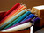 An array of hand-rolled beeswax mini candles in vibrant colors are angled to the side in a basket with a block of beeswax in the background.