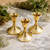 Three polished brass taper candle holders with concentric ring bases arranged on a light stone surface in a natural garden setting.
