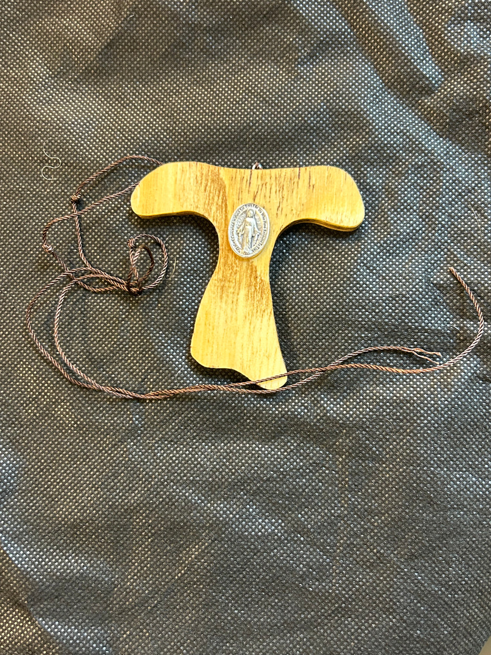 Rustic wooden hand crafted Tau Cross pendant, 3 1/2 inches tall with a Miraculous Medal, comes with a cord attached, wood grain varies. Rustic wooden hand crafted Tau Cross pendant, 3 1/2 inches tall with a Miraculous Medal, comes with a cord attached, wood grain varies.