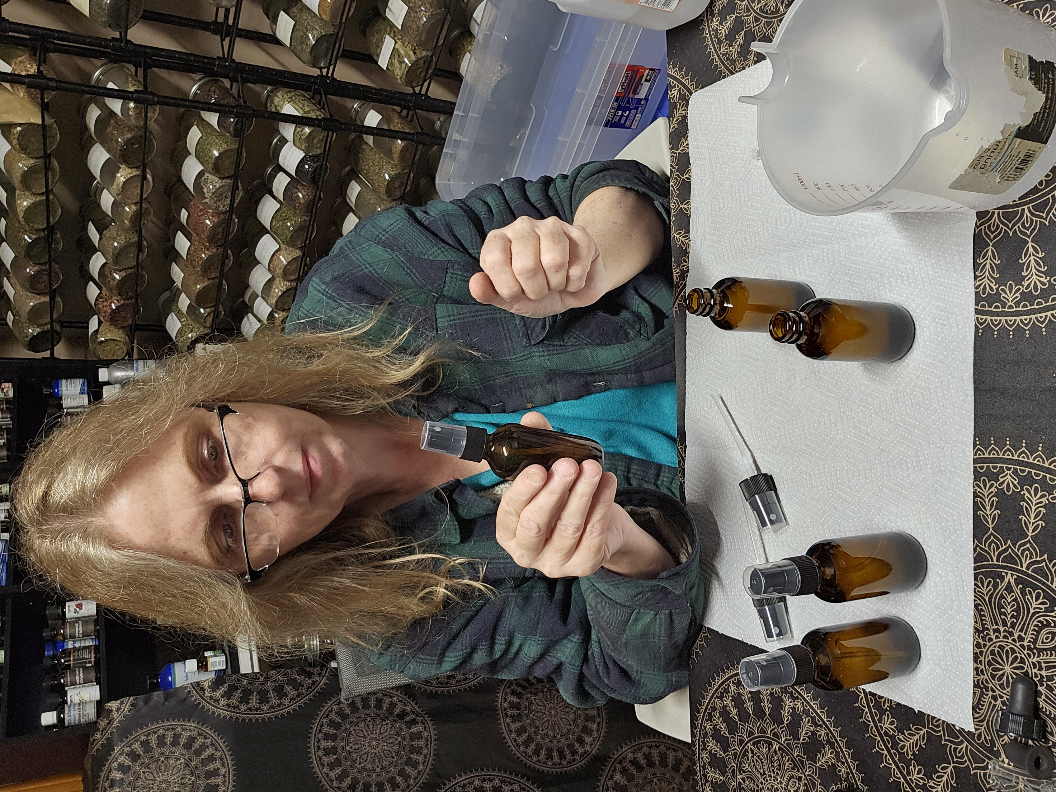 Bonnie Landsee bottling tinctures in her workspace with herb shelves behind her