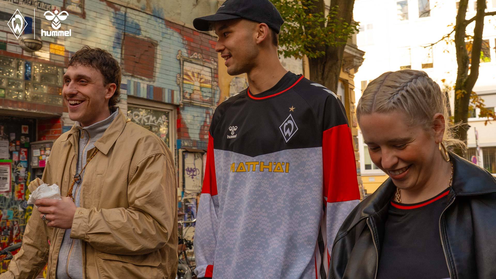 Drei Menschen laufen durch das Bremer Viertel. Einer davon ist Mio Backhaus, der das graue langarm Torwarttrikot trägt.