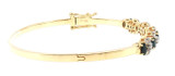 Side-angle view of an 18K yellow gold bangle showcasing its polished band, raised sapphire and diamond settings, and secure clasp with safety closures.