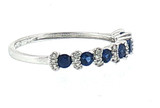 Angled side view highlighting the alternating royal blue sapphires and diamond accents across the top of the polished 18K white gold band.