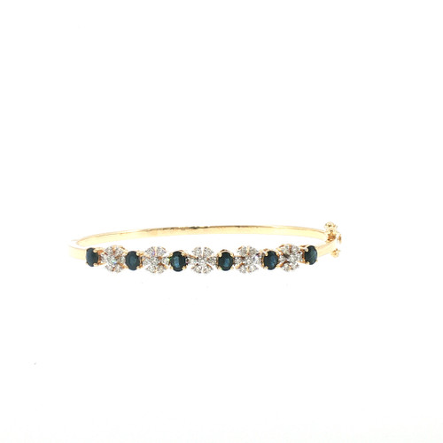 Front view of an 18K yellow gold bangle featuring alternating deep blue oval sapphires and sparkling floral diamond clusters totaling 0.68 ct of diamonds.