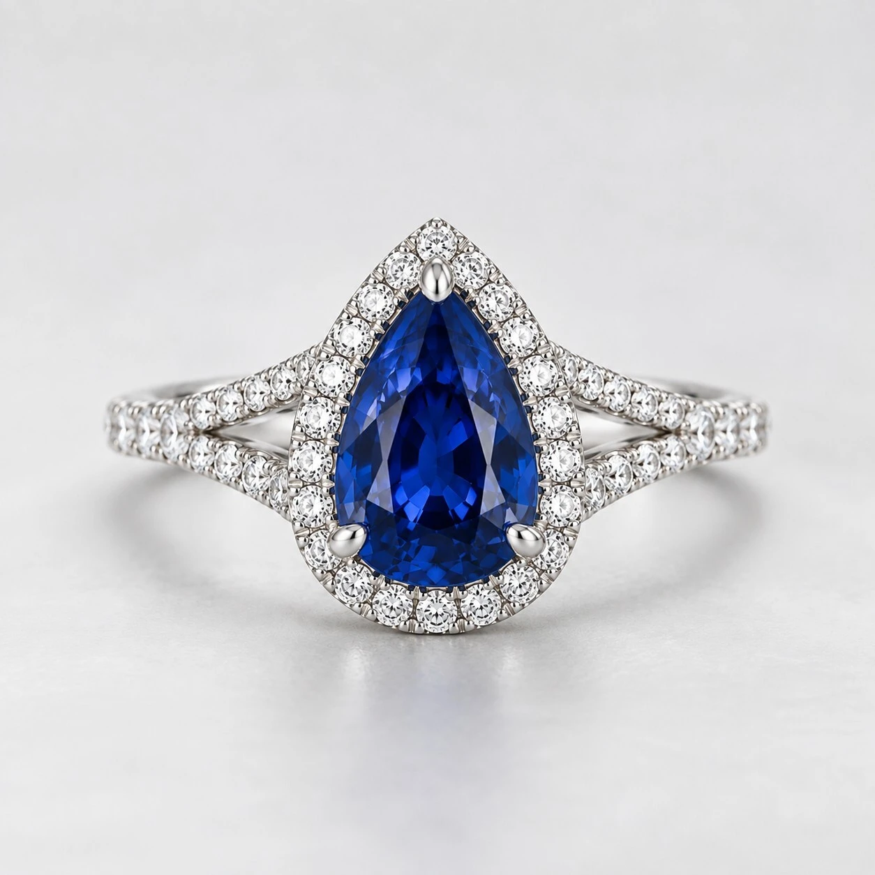 Pear-shaped blue sapphire engagement ring with diamond halo and split shank pave band