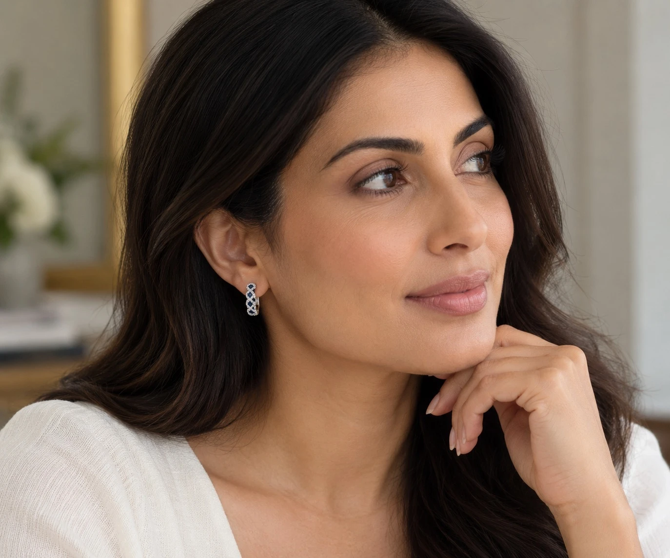 Woman wearing royal blue sapphire and diamond crisscross hoop earrings in 18K white gold, the September birthstone, at Karat 22 Jewelers in Houston