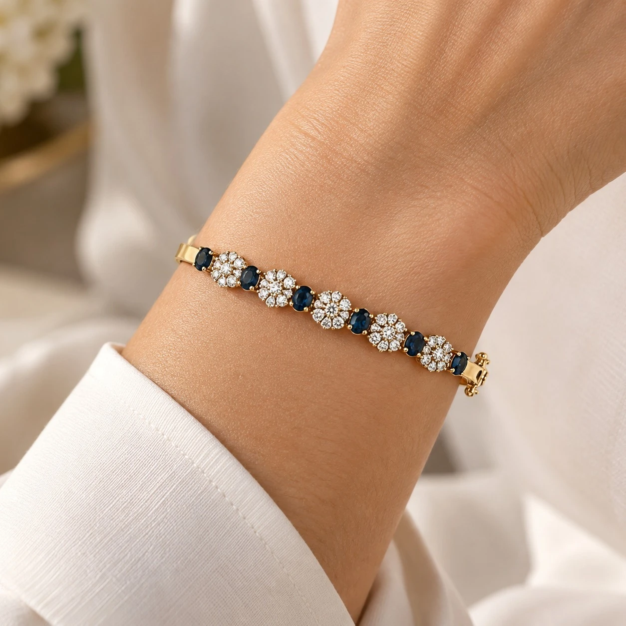 Woman wearing an alternating blue sapphire and diamond floral cluster bangle in 18K yellow gold