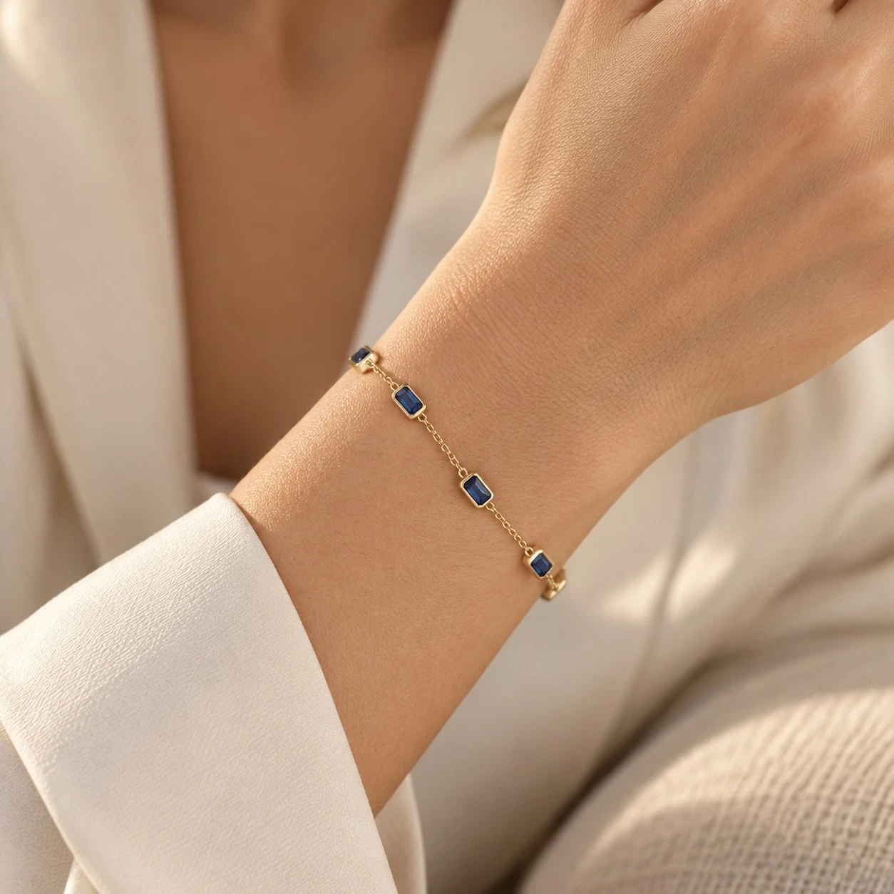 Woman wearing a deep blue sapphire station chain bracelet in 14K yellow gold on the wrist