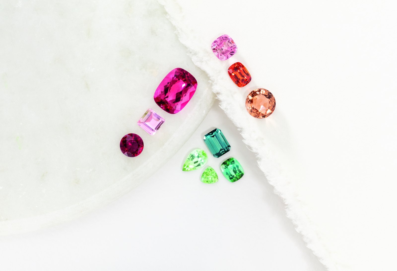 Loose tourmalines on white marble in hot pink, soft pink, red, peach, teal and green, showing the colour range of the gem