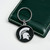 Michigan State Spartans NCAA Carved Metal Keychain - on a white table next to a green wallet
